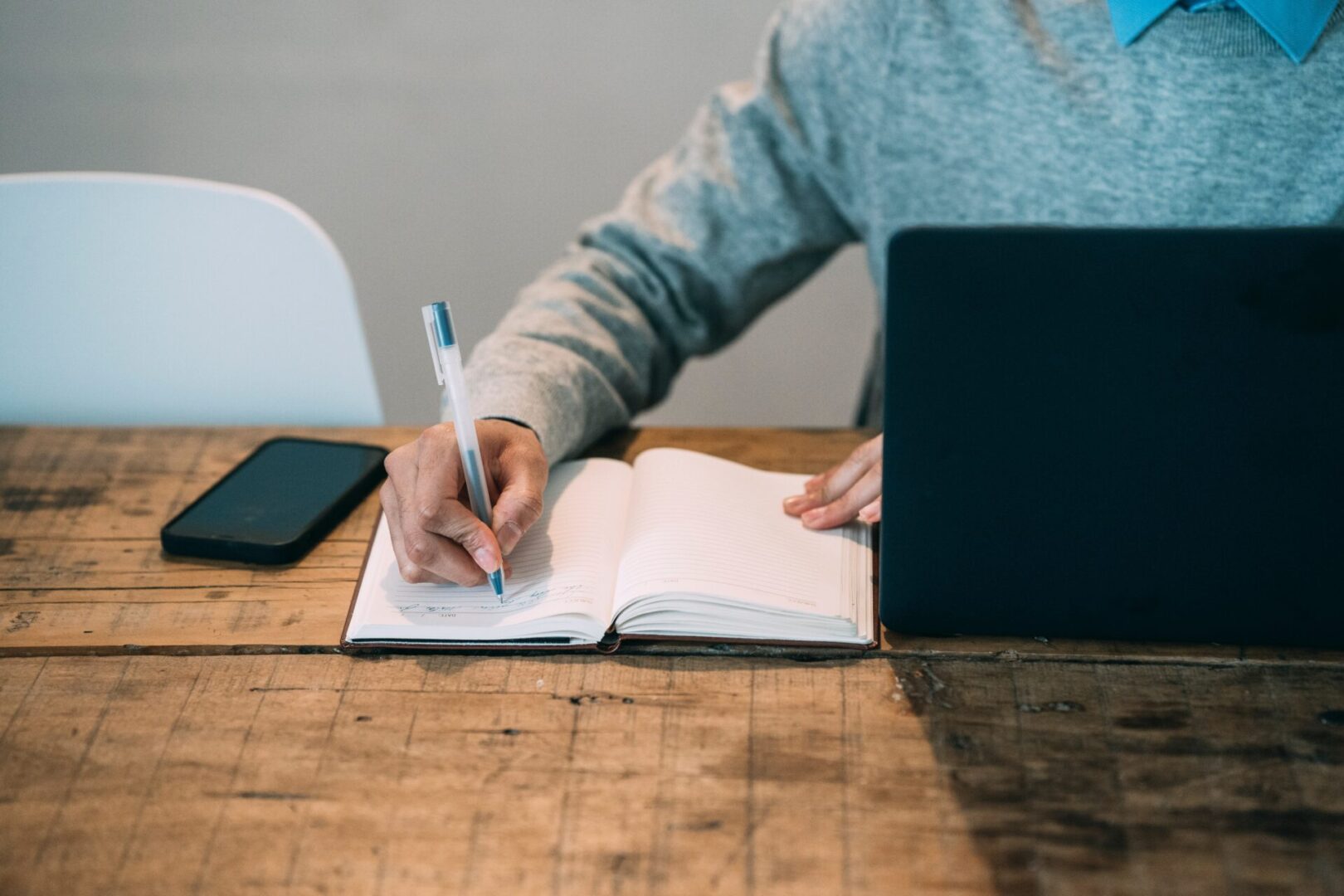 Person with laptop taking notes using pen on notebook